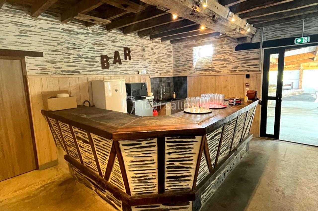 Bar en bois rustique avec comptoir décoré, boissons disposées, éclairage chaleureux et murs en pierre et bois.