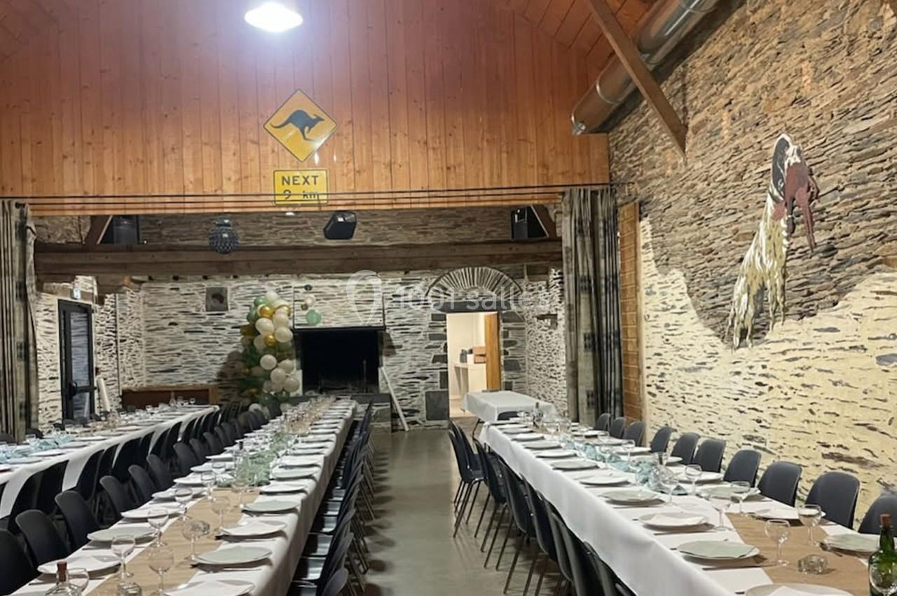 Salle de réception avec longues tables dressées, murs en pierre, décorations et un panneau mural jaune.