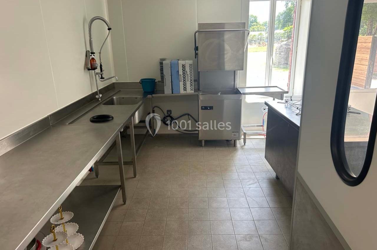 Cuisine professionnelle avec plans de travail en inox, évier, lave-vaisselle industriel et vue sur l'extérieur.