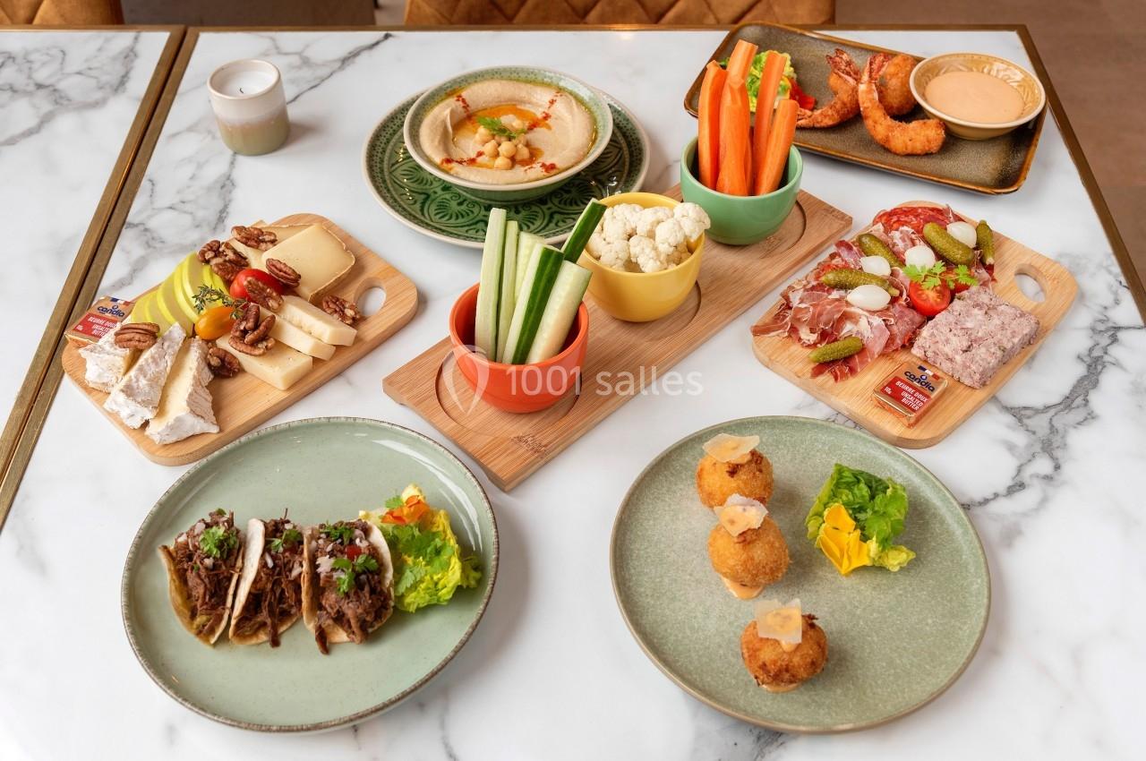 Assortiment de plats variés comprenant tapas, légumes, fromages, charcuteries, tacos et croquettes sur une table en marbre.