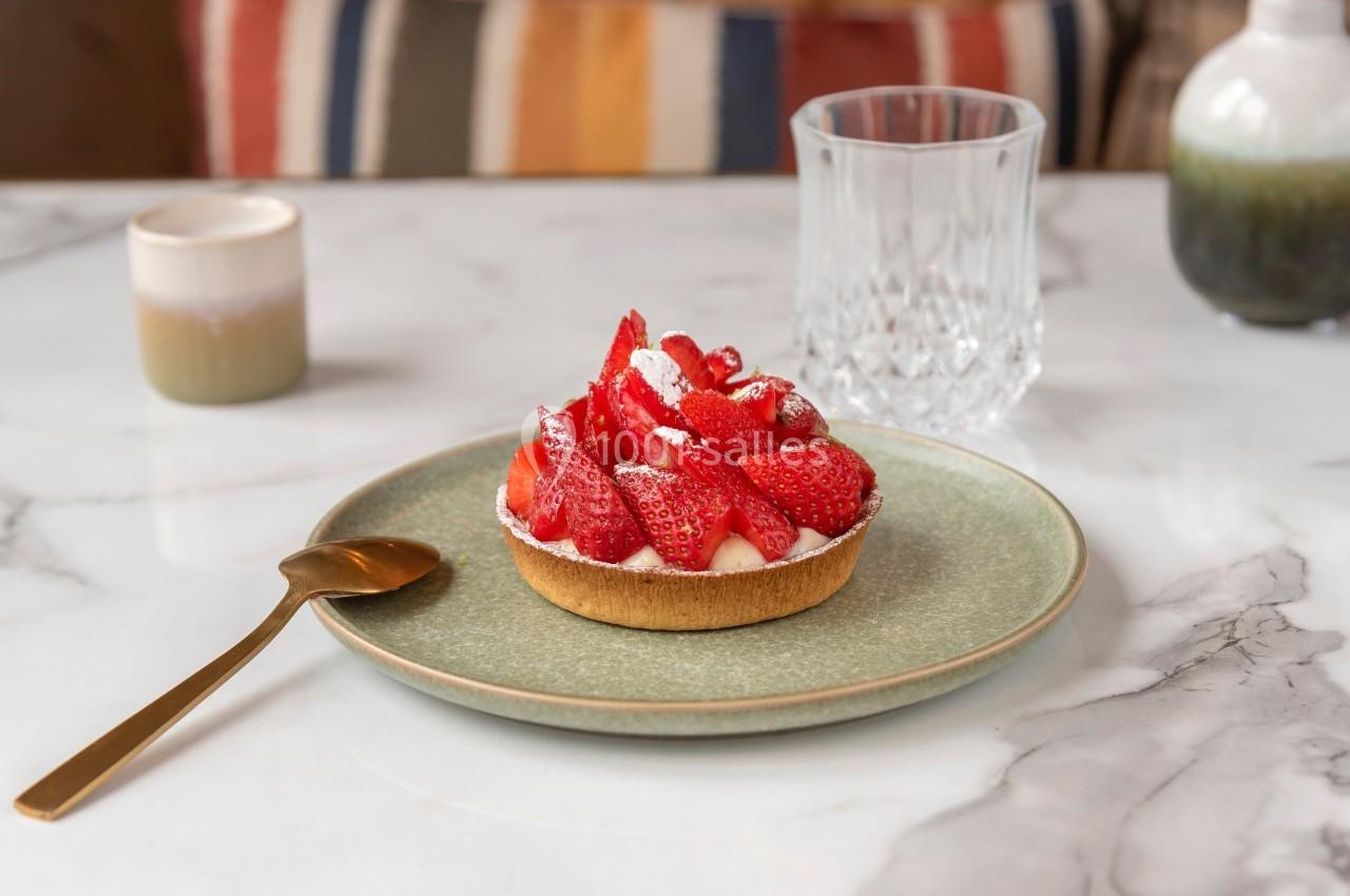 Tartelette aux fraises garnie de fruits frais et de sucre glace, servie sur une assiette verte avec une cuillère dorée.