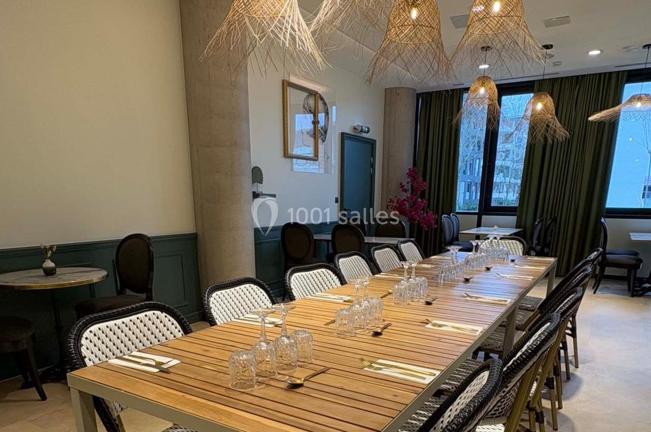 Salle de restaurant lumineuse avec une grande table en bois, chaises tressées et suspensions en fibres naturelles.