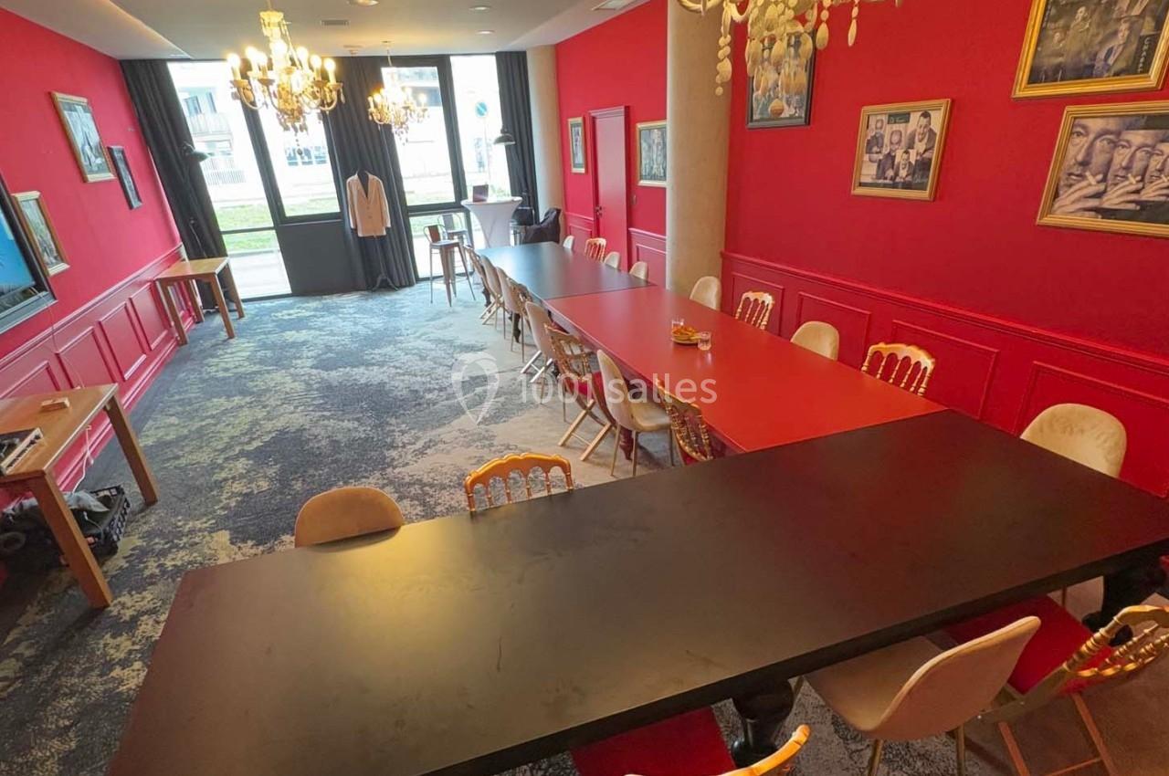Salle de réunion lumineuse avec murs rouges, grandes tables, chaises variées et décorations murales artistiques.