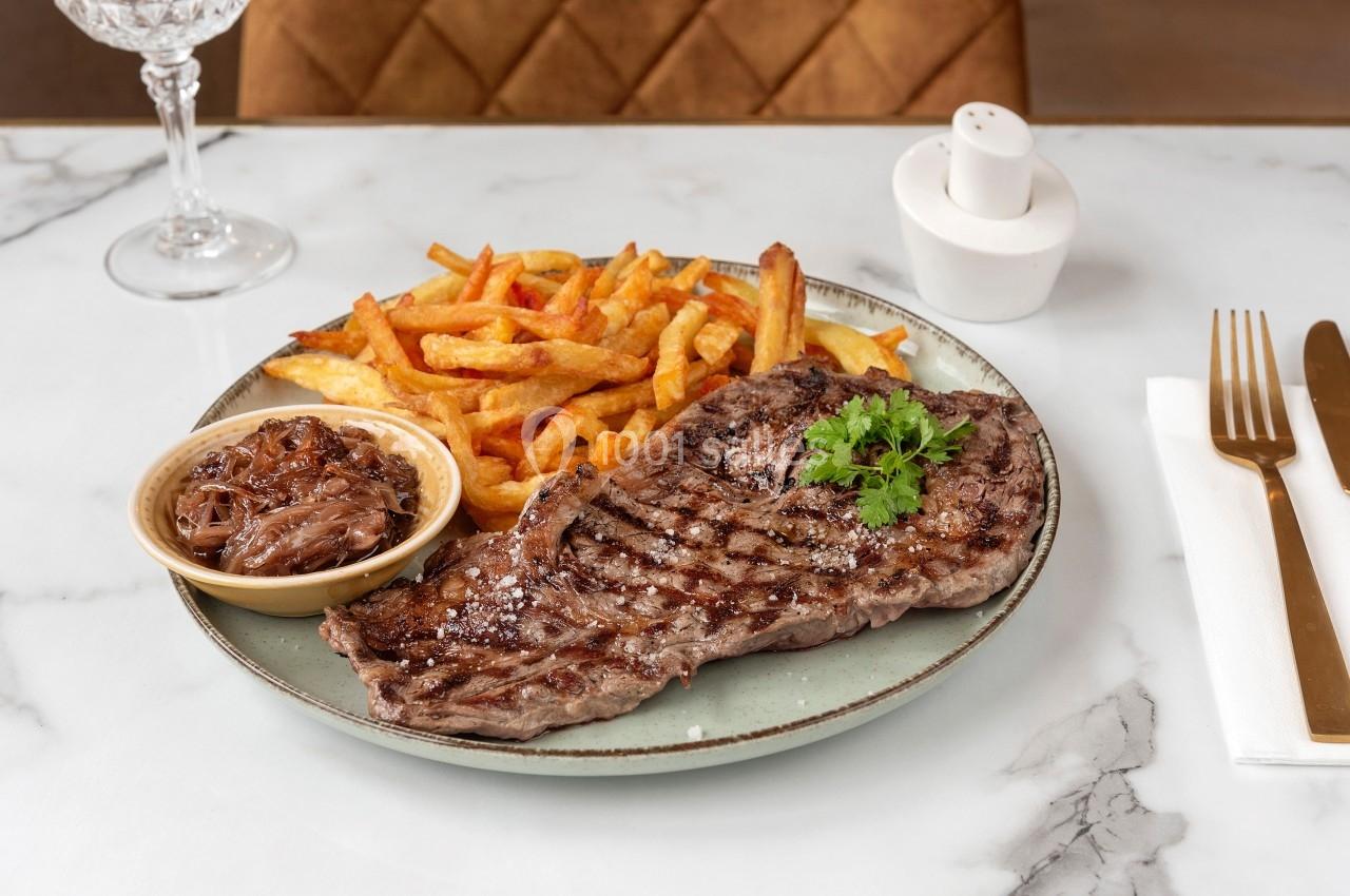 Assiette avec une entrecôte grillée, des frites dorées, un ramequin d'oignons confits et des couverts sur une table en…