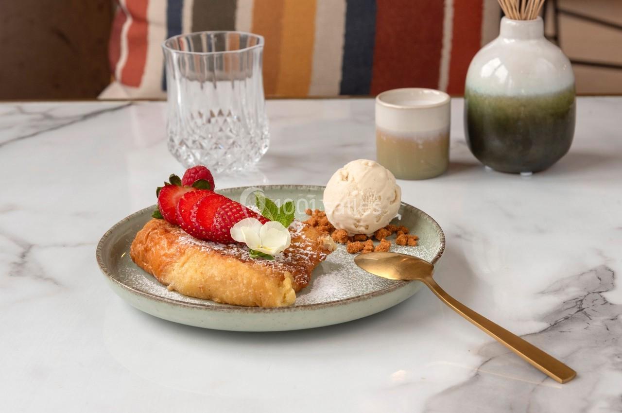 Assiette avec une pâtisserie garnie de fraises, crème glacée, miettes croustillantes et sucre glace, sur une table en marbre.