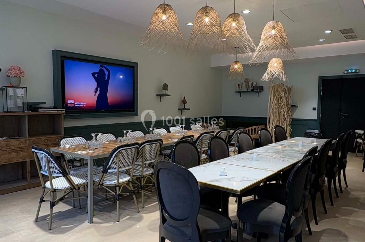 Salle de réunion lumineuse avec tables alignées, chaises variées, écran mural et suspensions en osier.