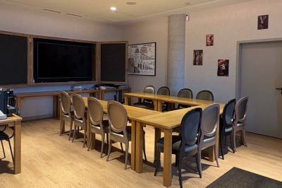 Salle de réunion avec une grande table en bois, entourée de fauteuils rembourrés, éclairée par une lampe et une fenêtre.