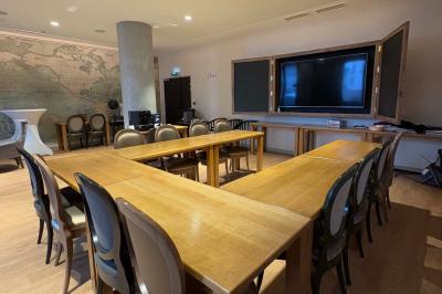 Salle de réunion avec une grande table en bois, entourée de fauteuils rembourrés, éclairée par une lampe et une fenêtre.