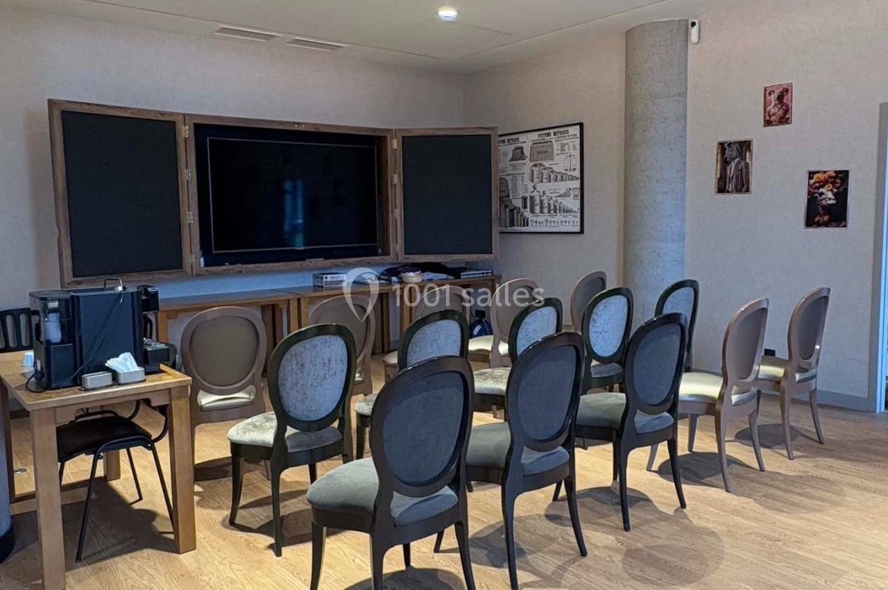 Salle équipée de chaises alignées face à un écran noir encadré, avec des éléments décoratifs sur les murs.