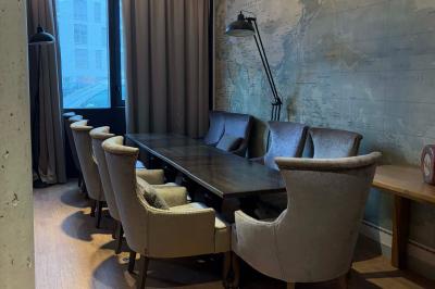 Salle de réunion avec une grande table en bois, entourée de fauteuils rembourrés, éclairée par une lampe et une fenêtre.