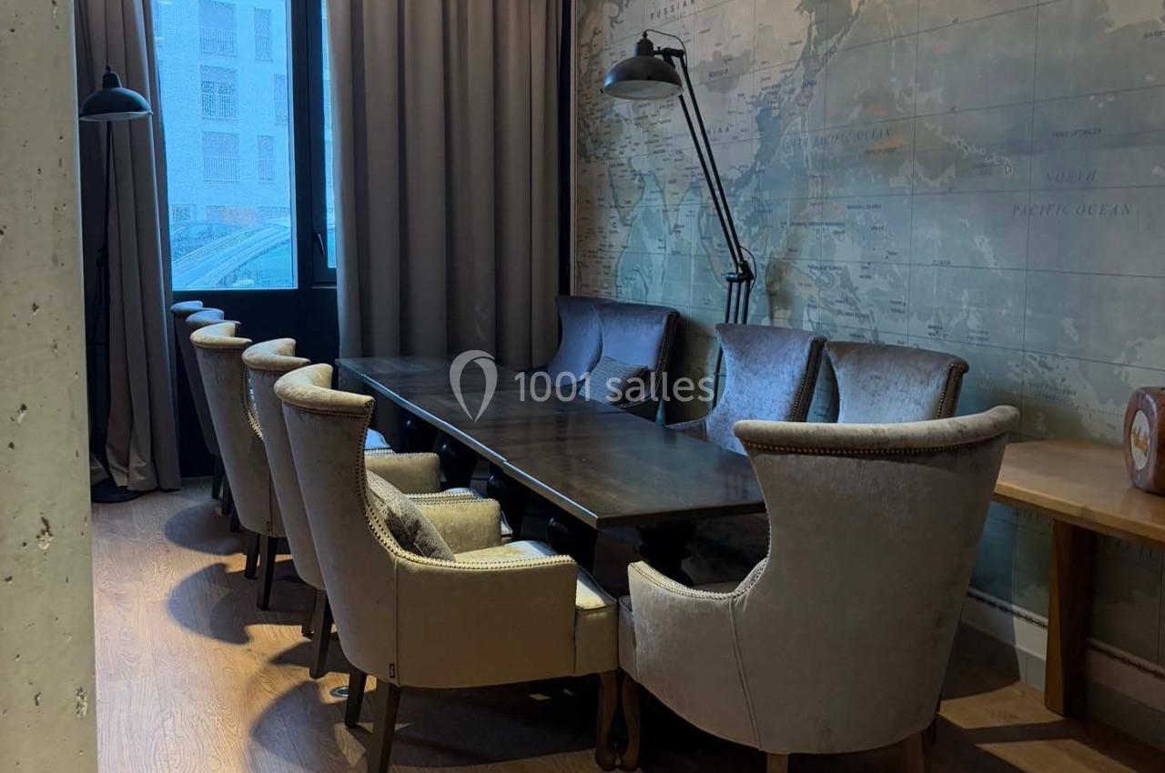 Salle de réunion avec une grande table en bois, entourée de fauteuils rembourrés, éclairée par une lampe et une fenêtre.