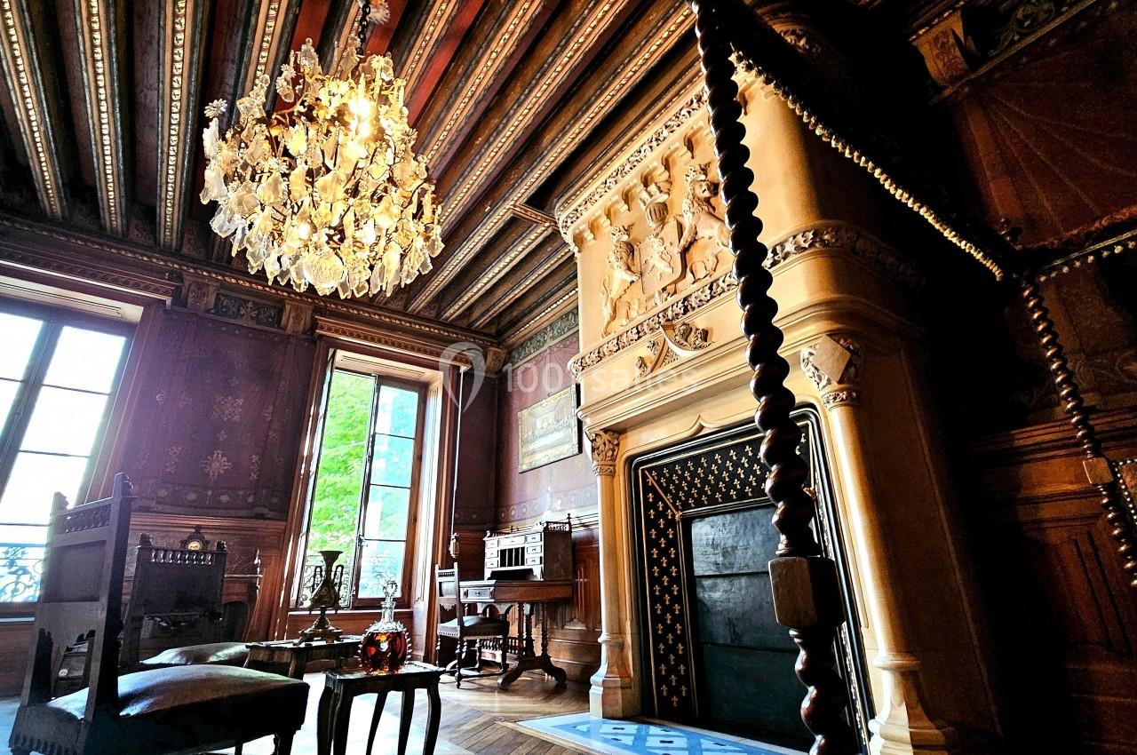 Salle historique avec cheminée sculptée, lustre en cristal, meubles anciens et plafond en bois décoré.