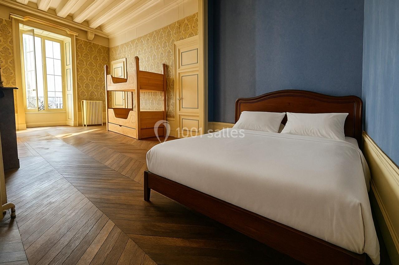 Chambre lumineuse avec un lit double, des lits superposés en bois, parquet en chevrons et murs bleus et jaunes.