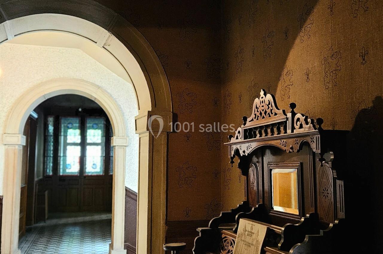 Un orgue ancien en bois sculpté est placé près d'une arche dans un couloir éclairé par une lumière naturelle.