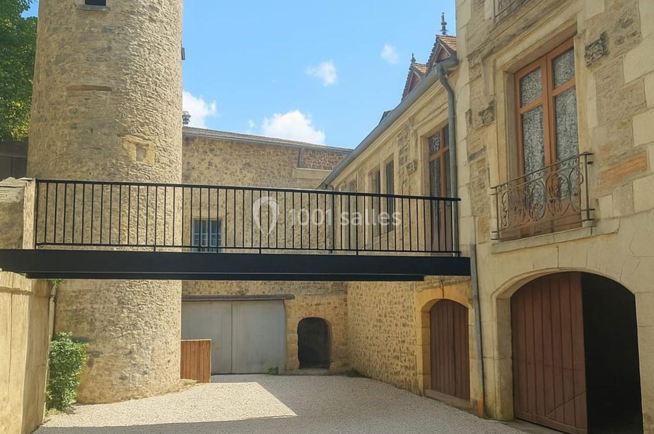 Cour intérieure avec une passerelle métallique reliant une tour en pierre et un bâtiment ancien aux façades restaurées.