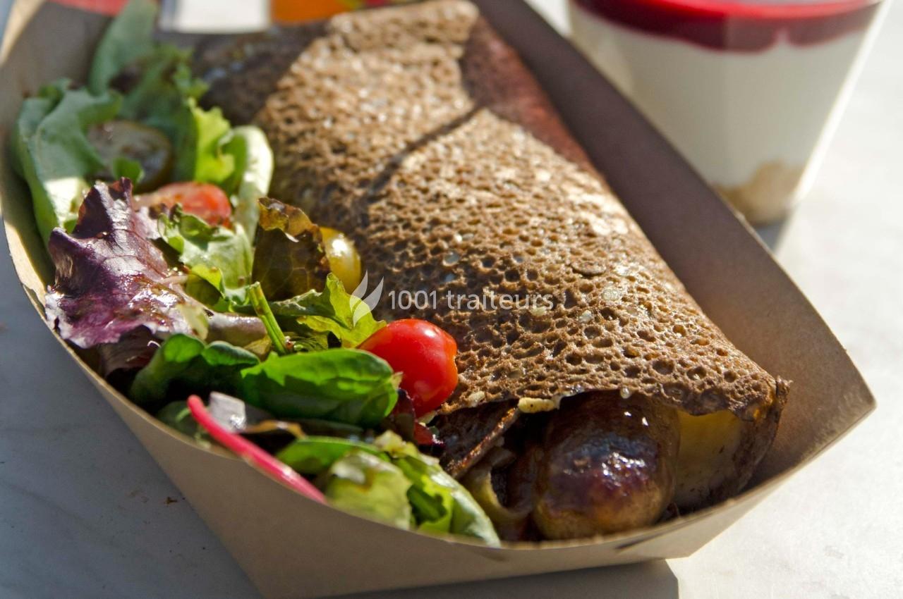 Galette de sarrasin garnie accompagnée d'une salade verte avec tomates cerises, servie dans une barquette en carton.