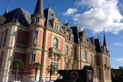 Façade d'un château en briques rouges et pierre claire avec tourelles, sous un ciel bleu partiellement nuageux.