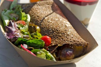Galette de sarrasin garnie accompagnée d'une salade verte avec tomates cerises, servie dans une barquette en carton.
