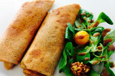 Deux galettes de sarrasin roulées accompagnées de mâche, d'une tomate cerise, de noix et d'une sauce.