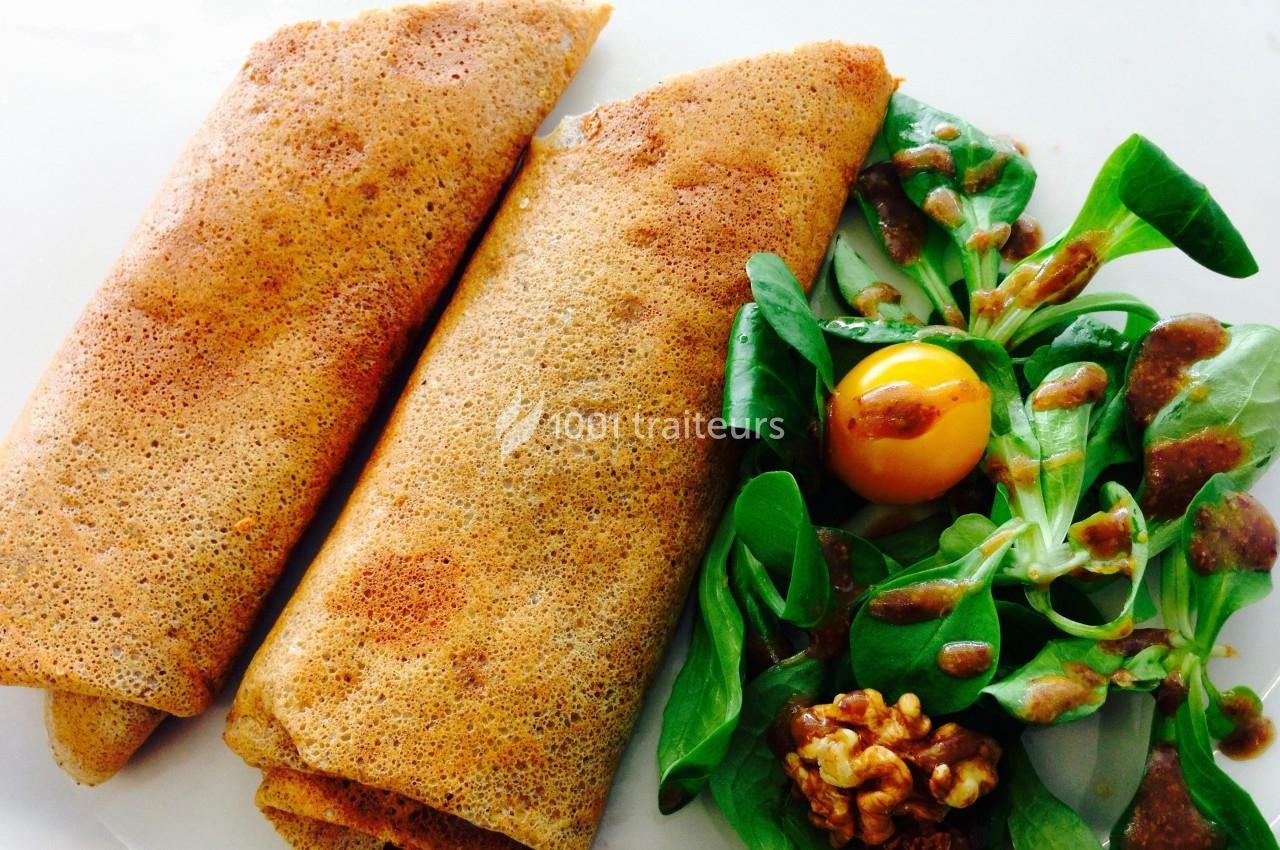 Deux galettes de sarrasin roulées accompagnées de mâche, d'une tomate cerise, de noix et d'une sauce.