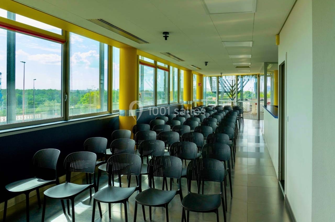 Location salle Caluire-et-Cuire (Rhône) - Le Belvédère #12 Salle lumineuse avec rangées de chaises noires alignées face à une fenêtre offrant une vue sur un paysage extérieur.