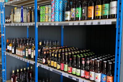 Étagères métalliques contenant diverses bouteilles d'alcool, alignées dans un entrepôt avec des cartons en dessous.