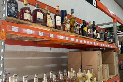 Étagères métalliques contenant diverses bouteilles d'alcool, alignées dans un entrepôt avec des cartons en dessous.