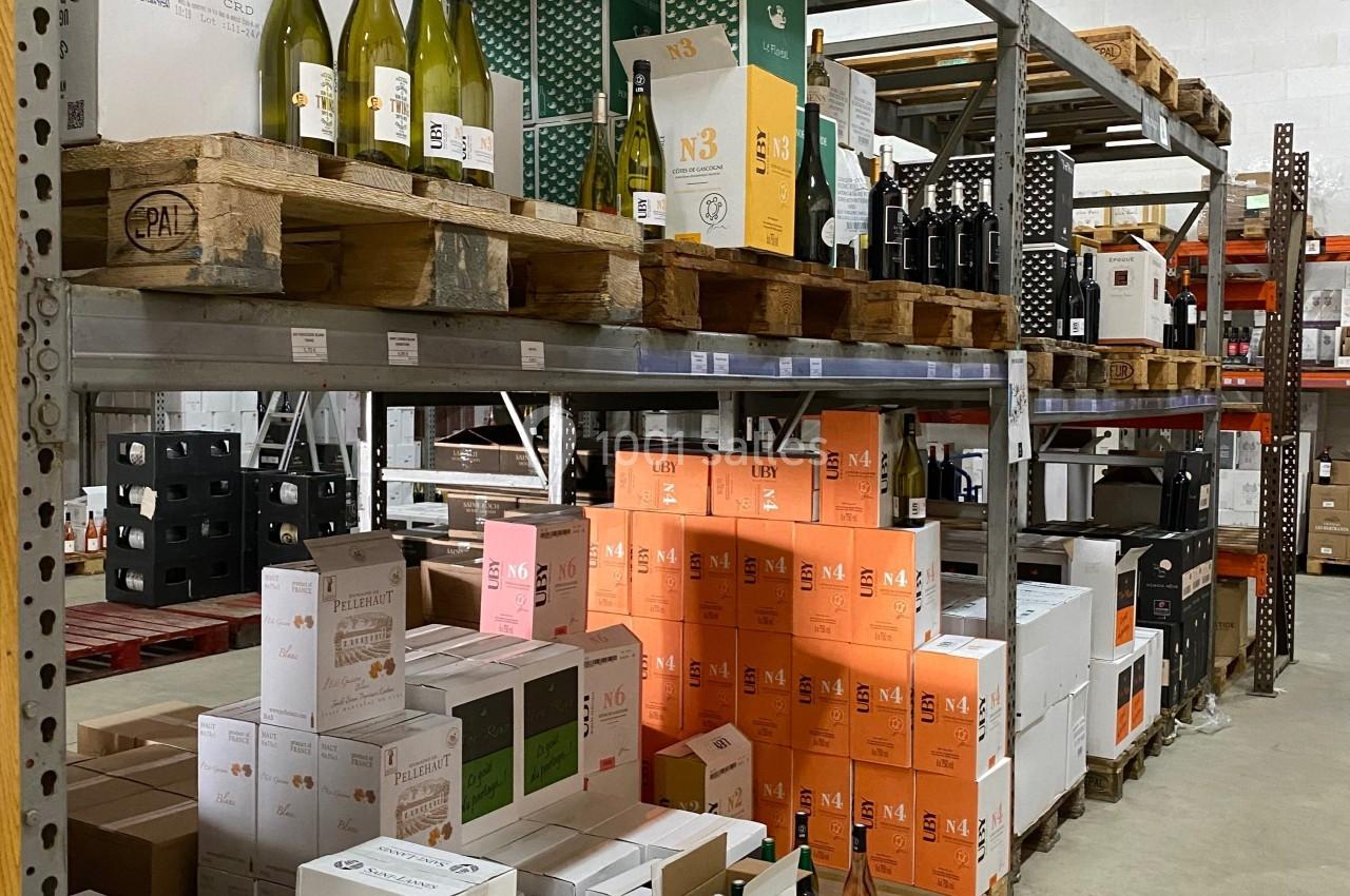 Rayonnages d'entrepôt avec des cartons de vin et quelques bouteilles exposées sur des palettes en bois.