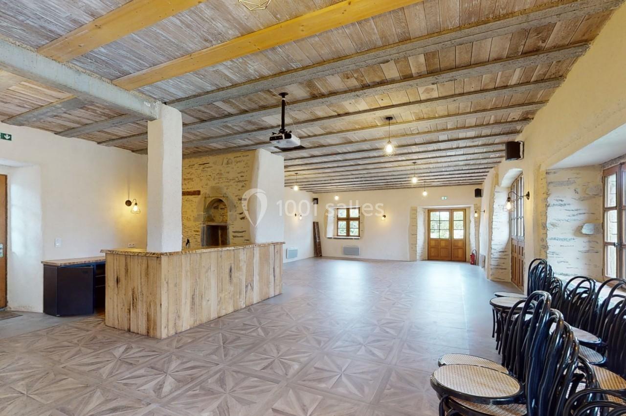 Salle lumineuse avec murs en pierre, plafond en bois, comptoir en bois et rangée de chaises noires empilées.
