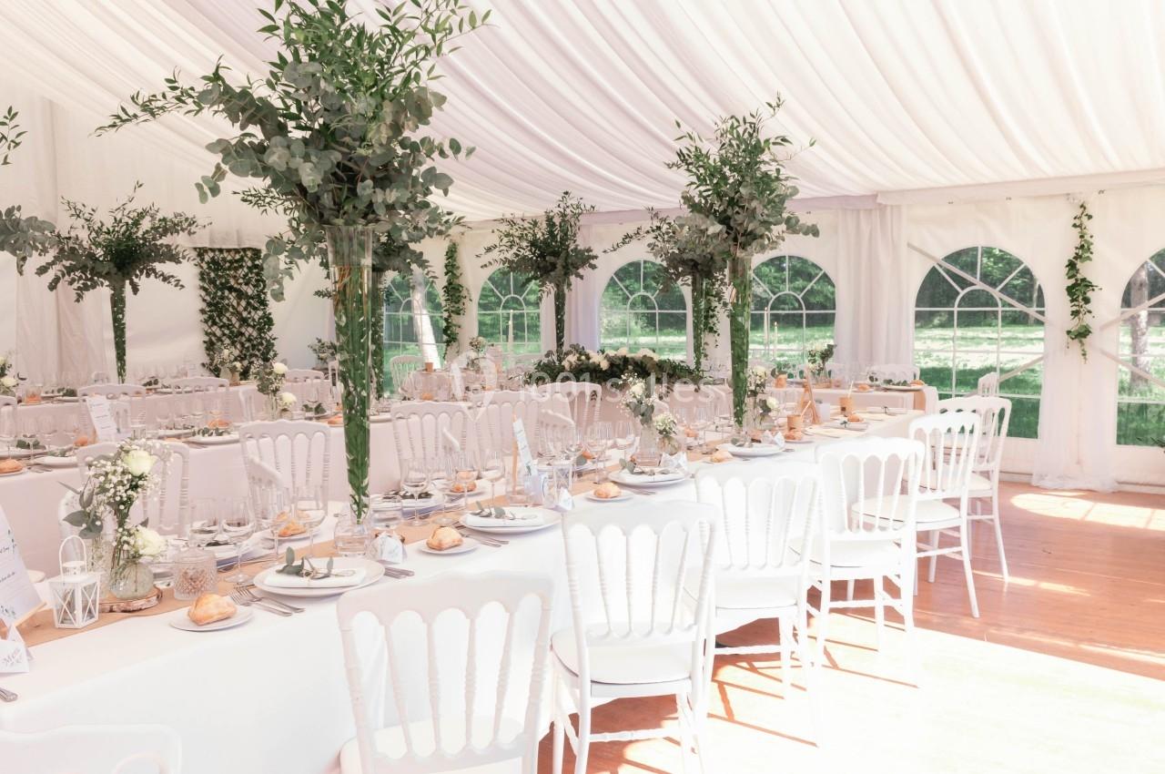 Salle de réception lumineuse sous une tente blanche, décorée de tables élégantes et de compositions florales.
