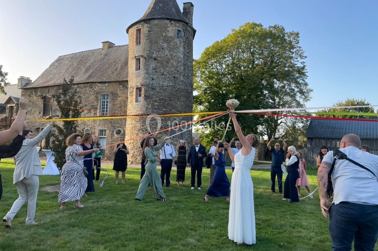 Des personnes participent à une danse traditionnelle avec des rubans colorés devant un manoir en pierre.