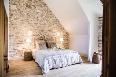 Chambre avec trois lits simples alignés, murs en pierre apparente, plafond en bois et lumière naturelle entrant par une…