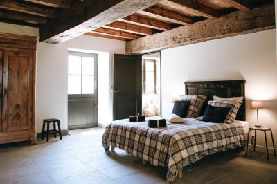 Chambre avec trois lits simples alignés, murs en pierre apparente, plafond en bois et lumière naturelle entrant par une…
