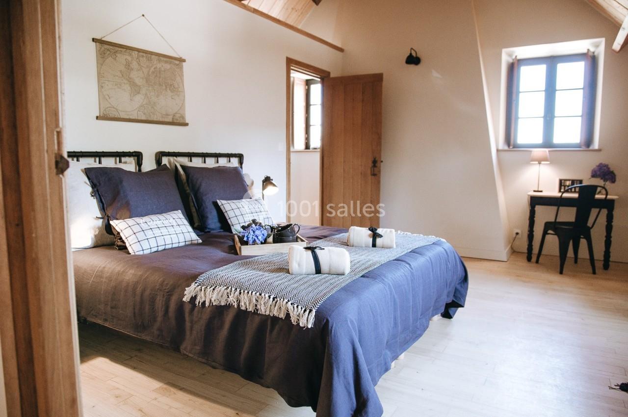 Chambre lumineuse avec lit double, draps bleus, bureau en bois près d'une fenêtre et décoration murale minimaliste.