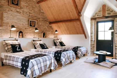 Chambre avec trois lits simples alignés, murs en pierre apparente, plafond en bois et lumière naturelle entrant par une…