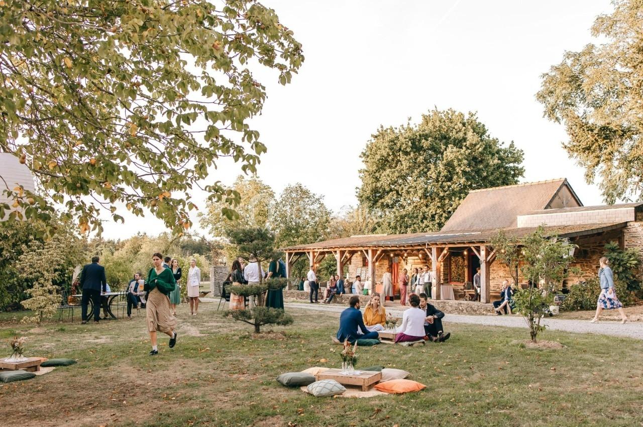 Des personnes discutent et se détendent dans un jardin verdoyant près d'un bâtiment en bois par une journée ensoleillée.