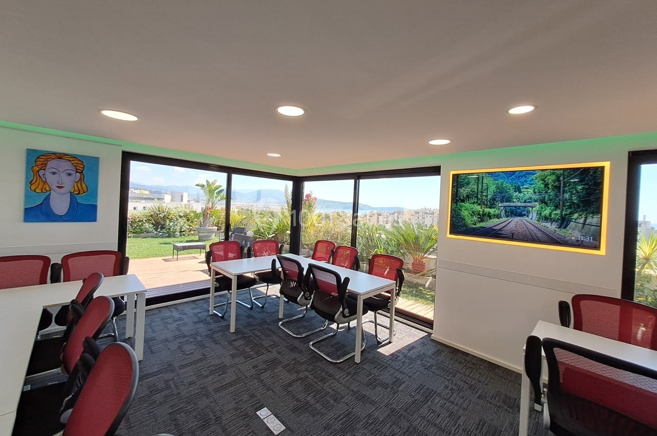 Salle de réunion lumineuse avec baies vitrées, vue sur une terrasse végétalisée et décorations murales colorées.