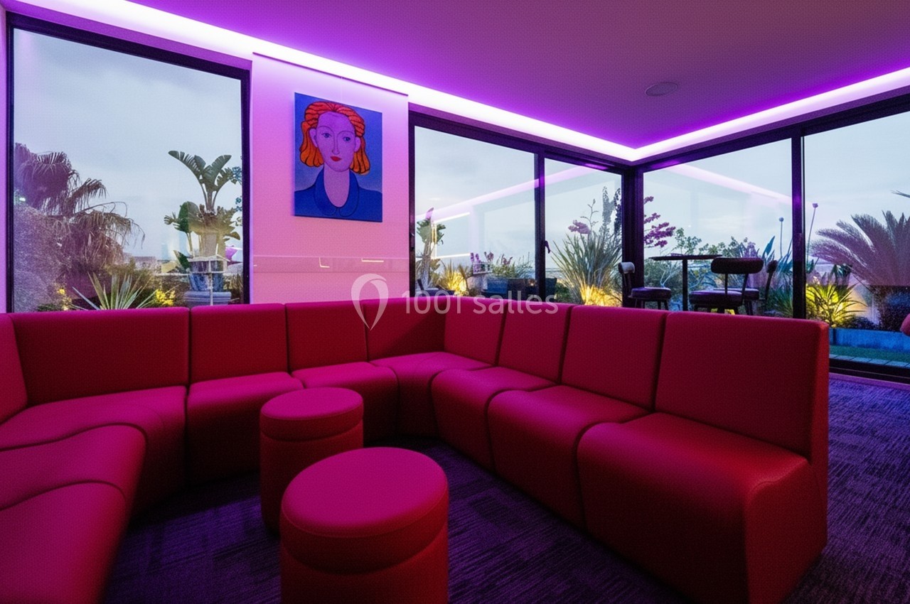 Salon moderne avec canapé rouge en angle, éclairage LED violet et grandes baies vitrées donnant sur un jardin.