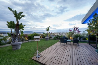 Terrasse avec pelouse, plantes en pots, mobilier de jardin et vue dégagée sur un paysage urbain et montagneux.