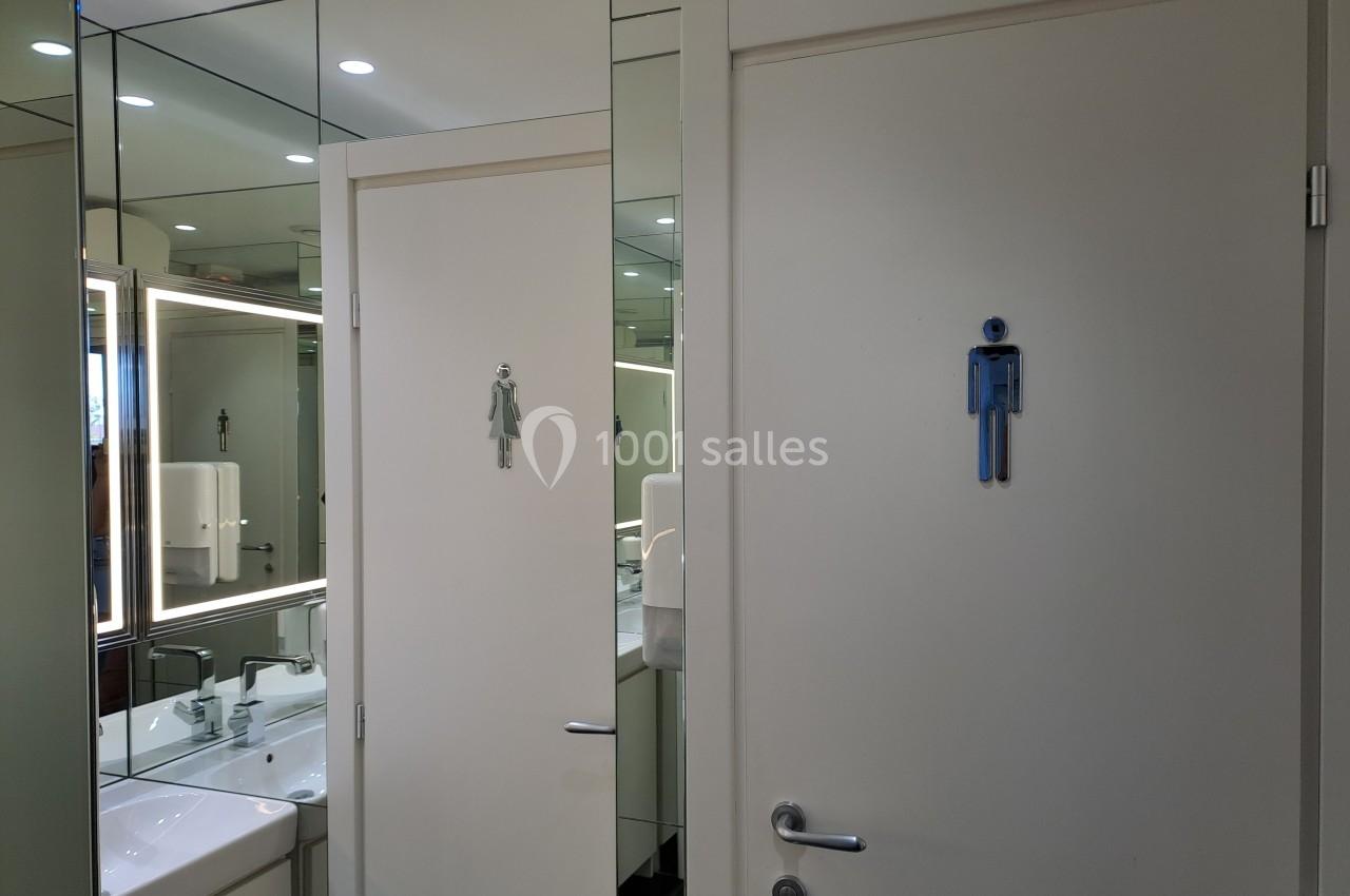 Deux portes de toilettes avec pictogrammes homme et femme, entourées de miroirs reflétant un lavabo.