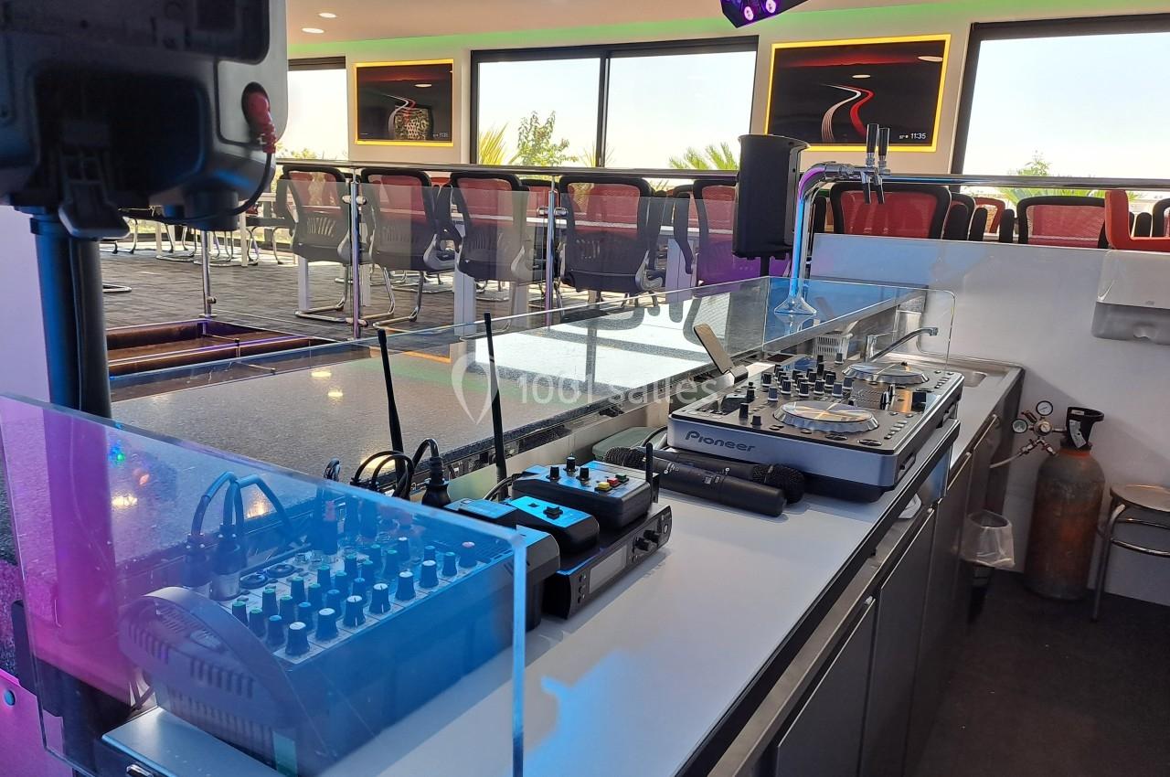 Poste de DJ équipé de platines, table de mixage et matériel audio, situé dans un espace lumineux avec des sièges en arrière…