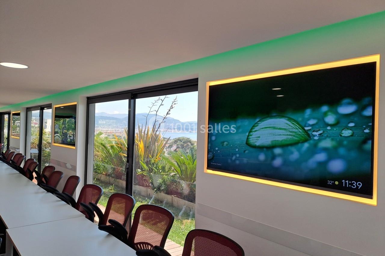 Salle de réunion lumineuse avec des écrans affichant une image de goutte d'eau et vue sur un paysage extérieur.