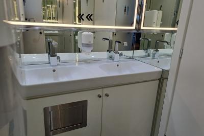 Double lavabo moderne avec robinets chromés, distributeur de savon mural et grand miroir éclairé en arrière-plan.