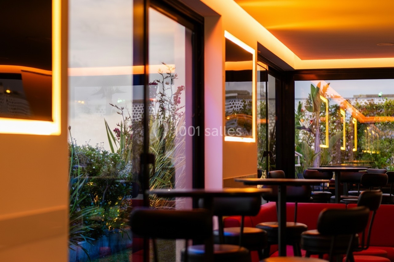 Salle moderne avec grandes baies vitrées, éclairage chaleureux et vue sur un jardin extérieur.