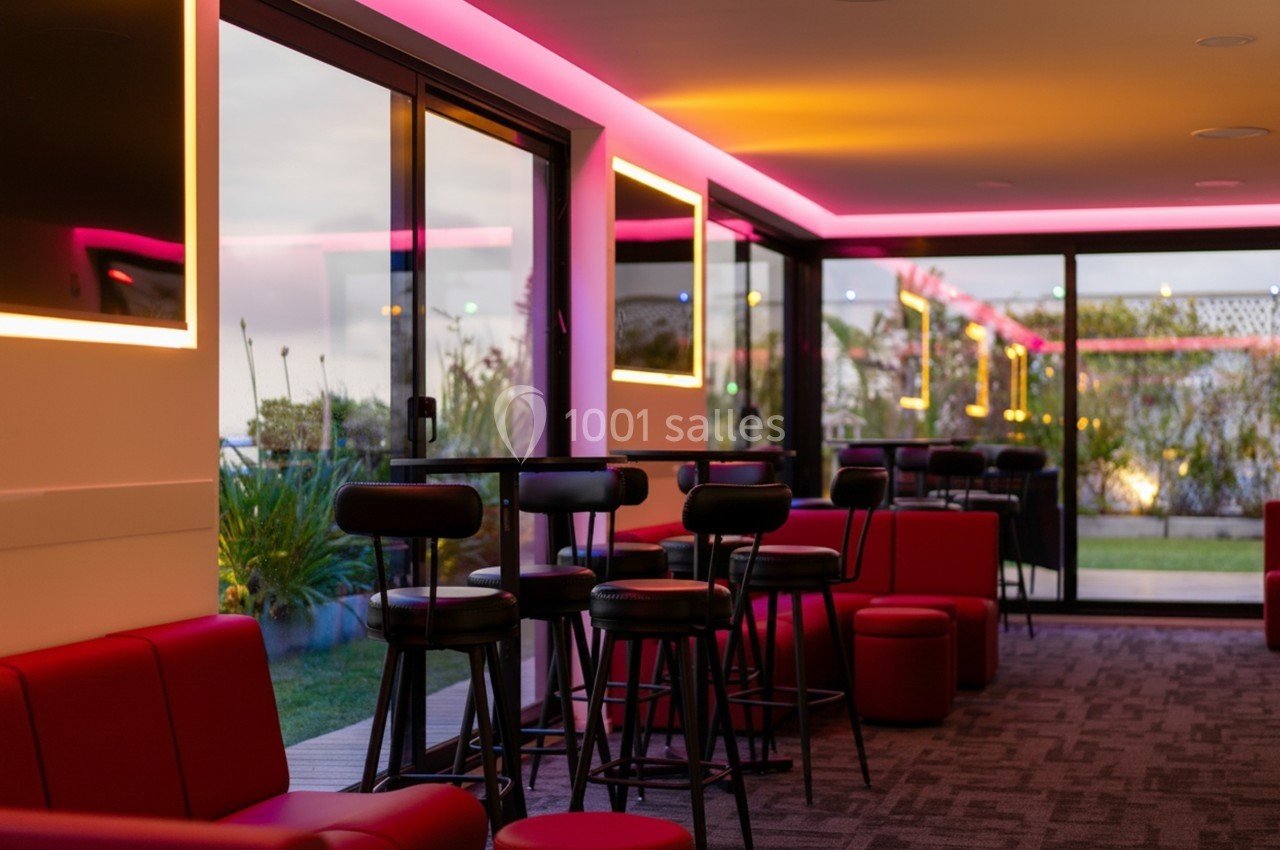 Salle moderne avec éclairage LED rose, mobilier noir et rouge, grandes baies vitrées donnant sur un espace extérieur.