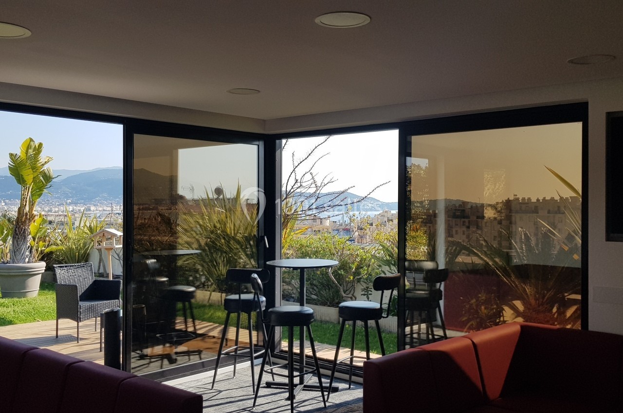 Salon lumineux avec baies vitrées donnant sur une terrasse, des plantes et une vue sur des montagnes.