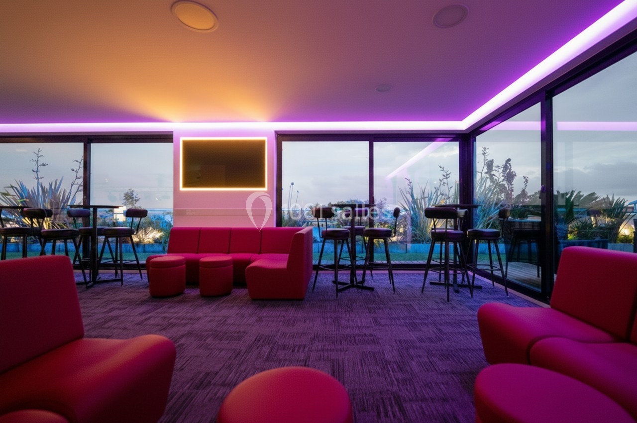 Salle moderne avec éclairage LED violet, mobilier rouge et grandes baies vitrées donnant sur un jardin.