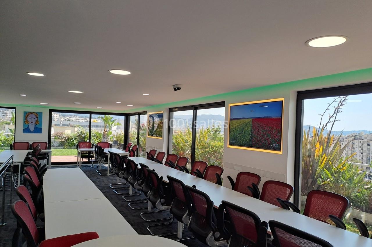 Salle de réunion lumineuse avec de grandes baies vitrées, des chaises rouges et des tableaux colorés sur les murs.