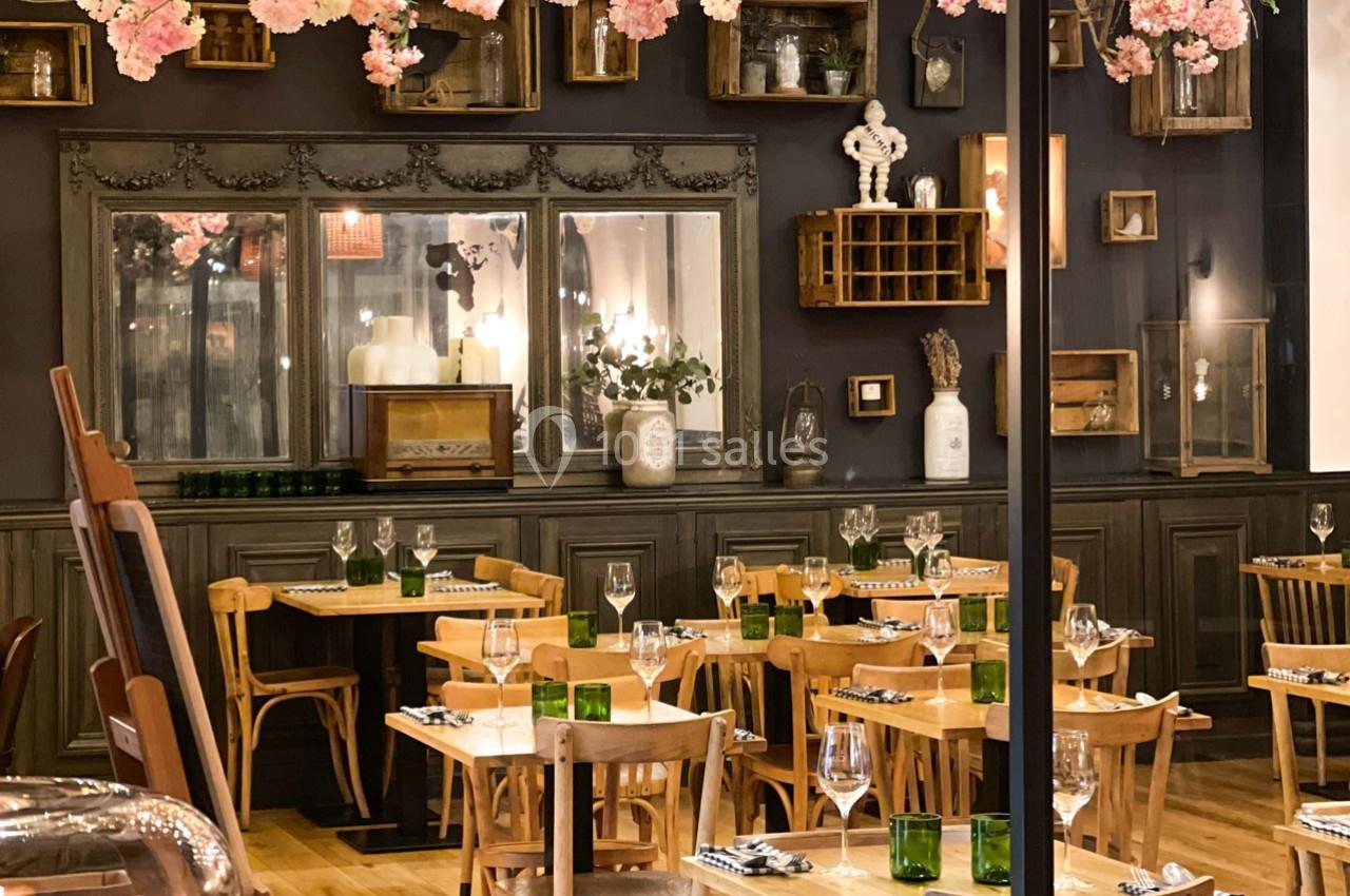 Salle de restaurant chaleureuse avec tables en bois, décoration vintage et fleurs suspendues.