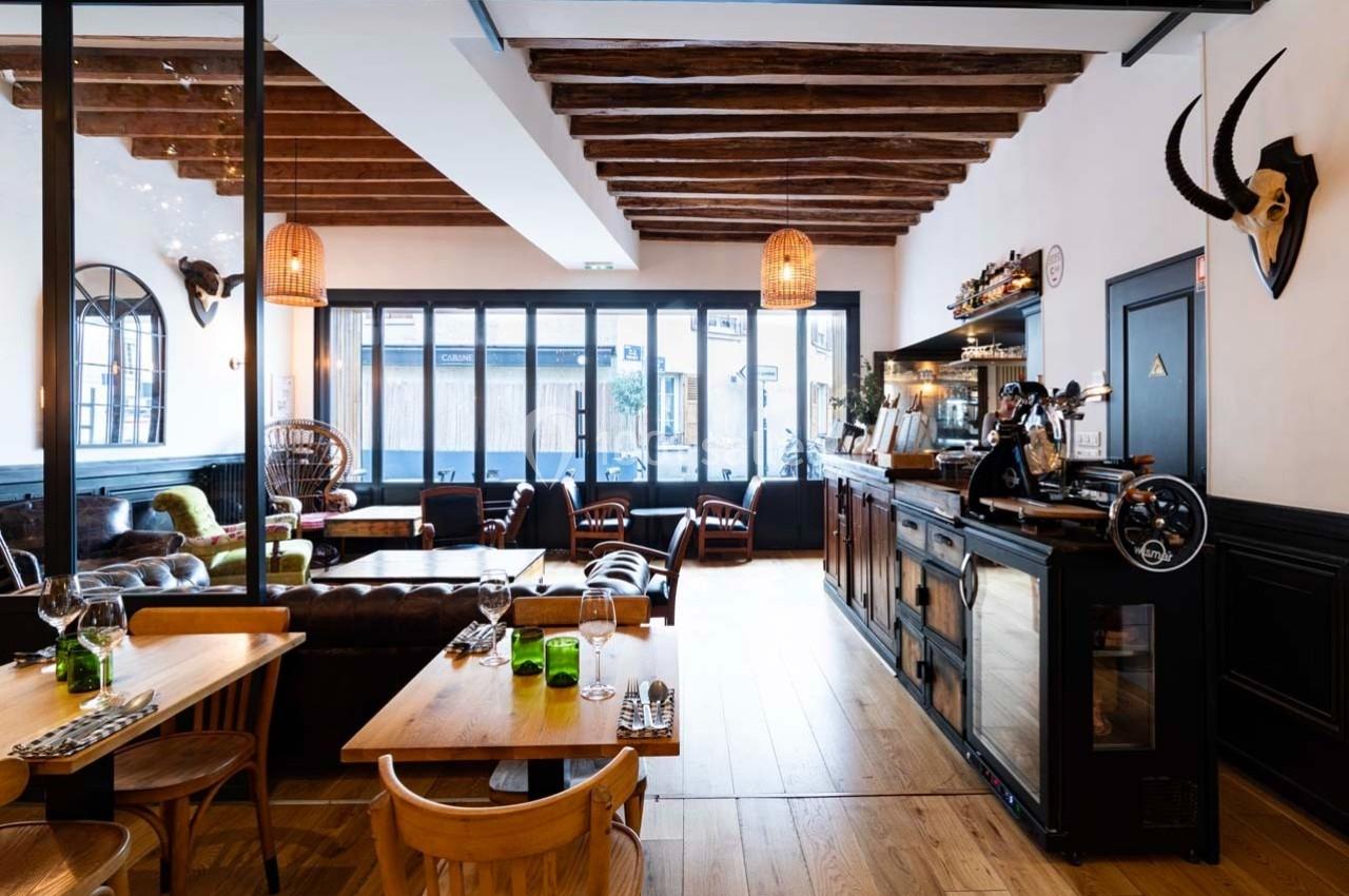 Salle de restaurant lumineuse avec mobilier en bois, grandes baies vitrées et décoration murale éclectique.